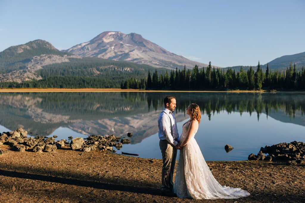 bride and groom walking along the shore of Sparks Lake with mountain views in Oregon