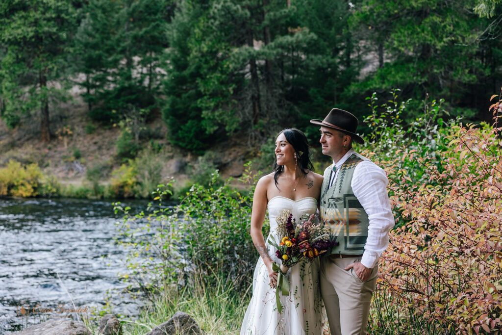 bride and groom standing by a river with a forest in the background