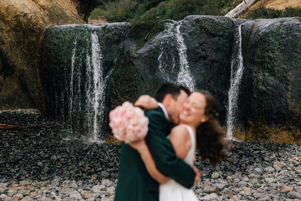 bride and groom in front of a small waterfall at oregon coast