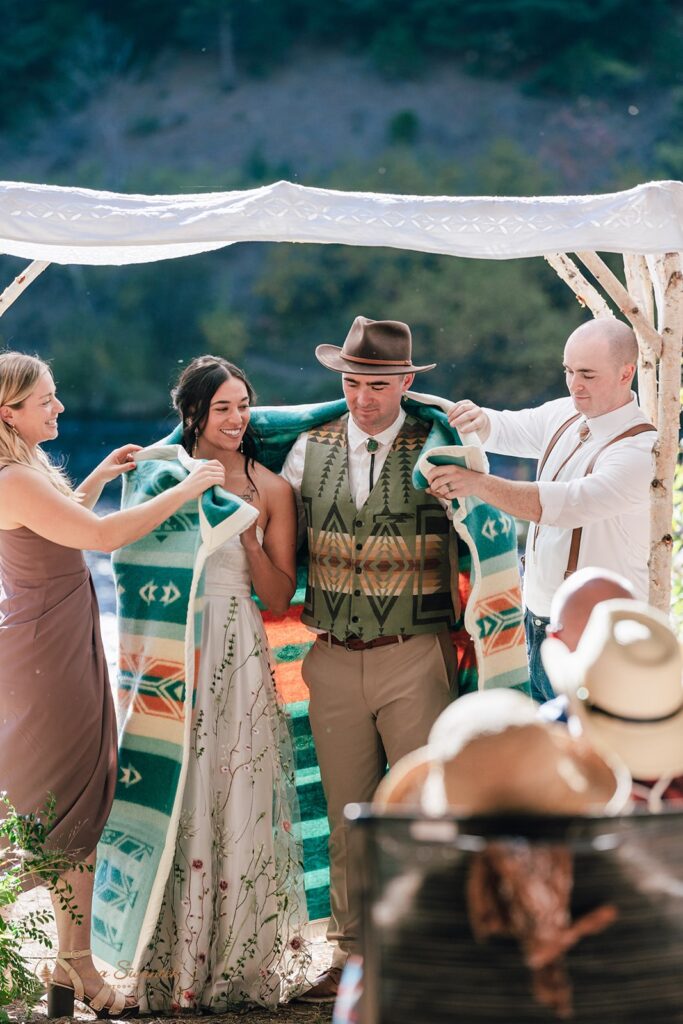 bride and groom getting wrapped up in a colorful blanket together during their wedding ceremony ritual