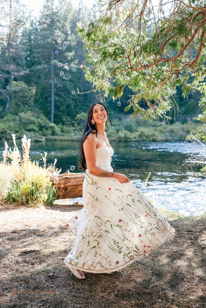 joyful bride twirling around in her floral embroidered wedding dress along the river