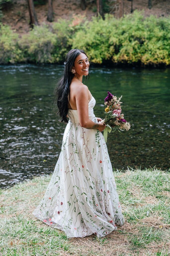 joyful bride twirling around in her floral embroidered wedding dress along the river