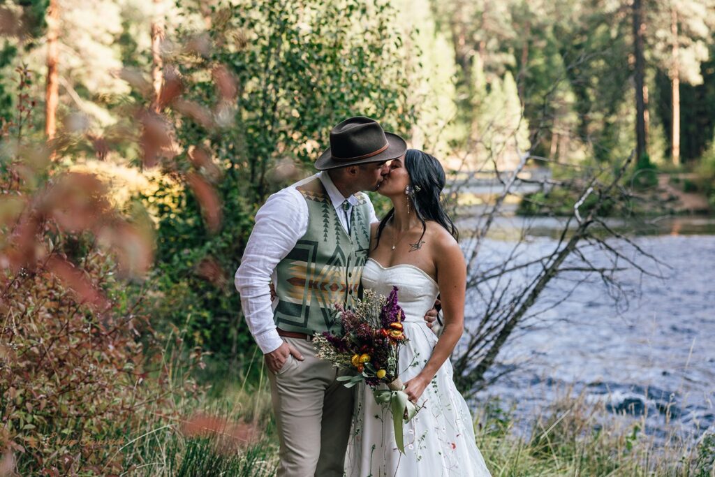 bride and groom kissing next to metolius river