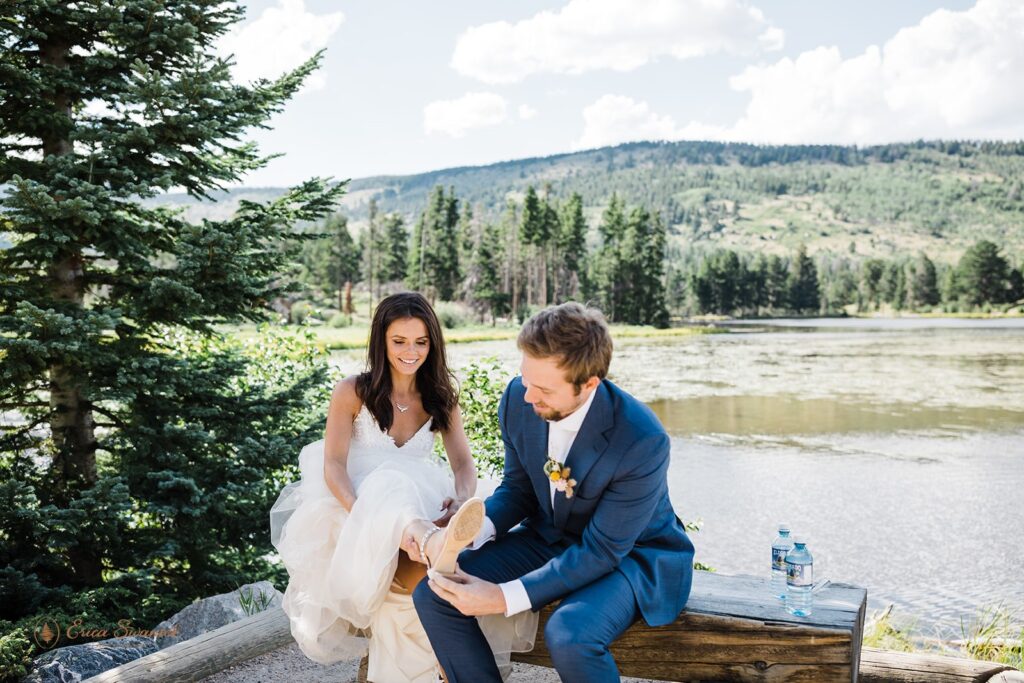 groom helping his bride put on her shoes during their rocky mountain national park elopement in sprague lake
