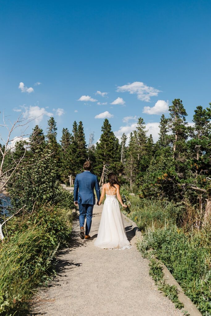 bride and groom walking hand in hand along a trail in sprague lake area in rocky mountain national park