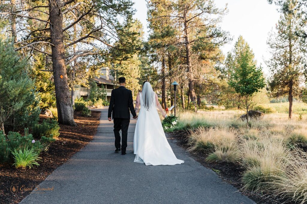 bride and groom walking hand in hand on a path towards sunriver resort