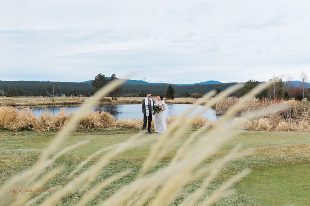 bride and groom standing in a wide open field with water and mountain views behind them during their Sunriver Resort wedding day