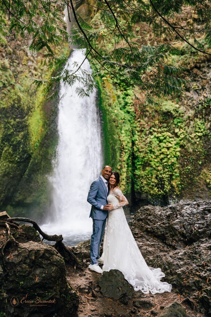 Bride and groom stand in front of a waterfall in Oregon