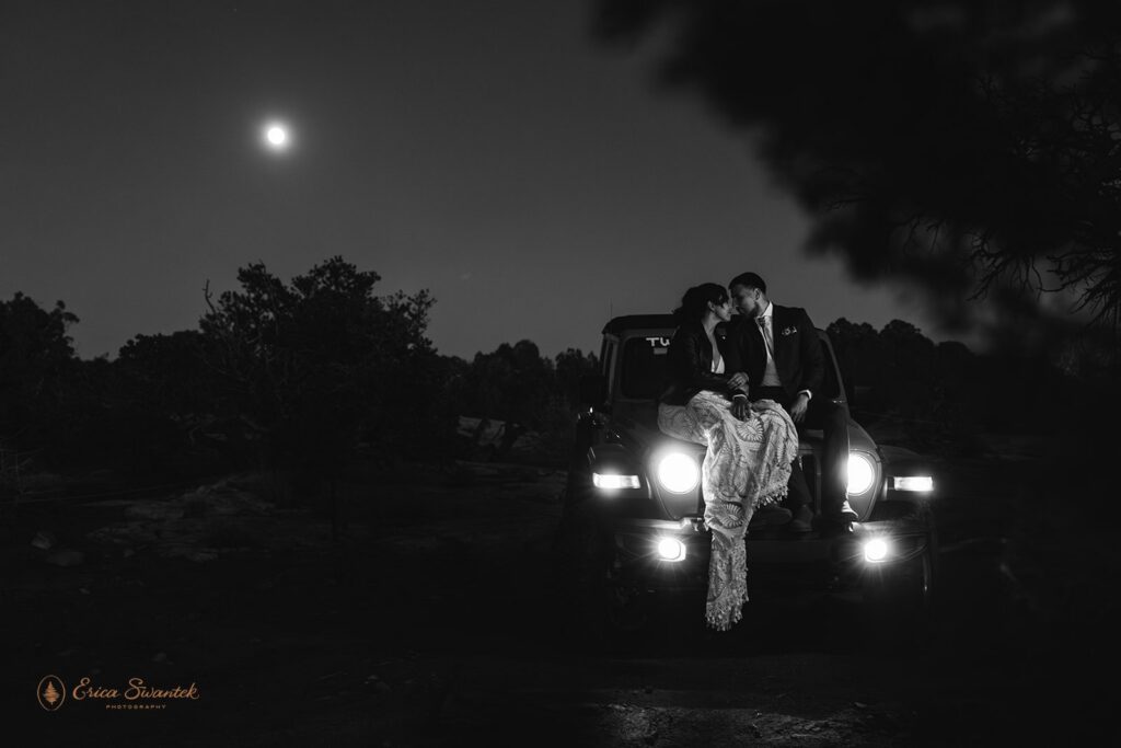 bride and groom sitting on the hood of the jeep with full moon in the background