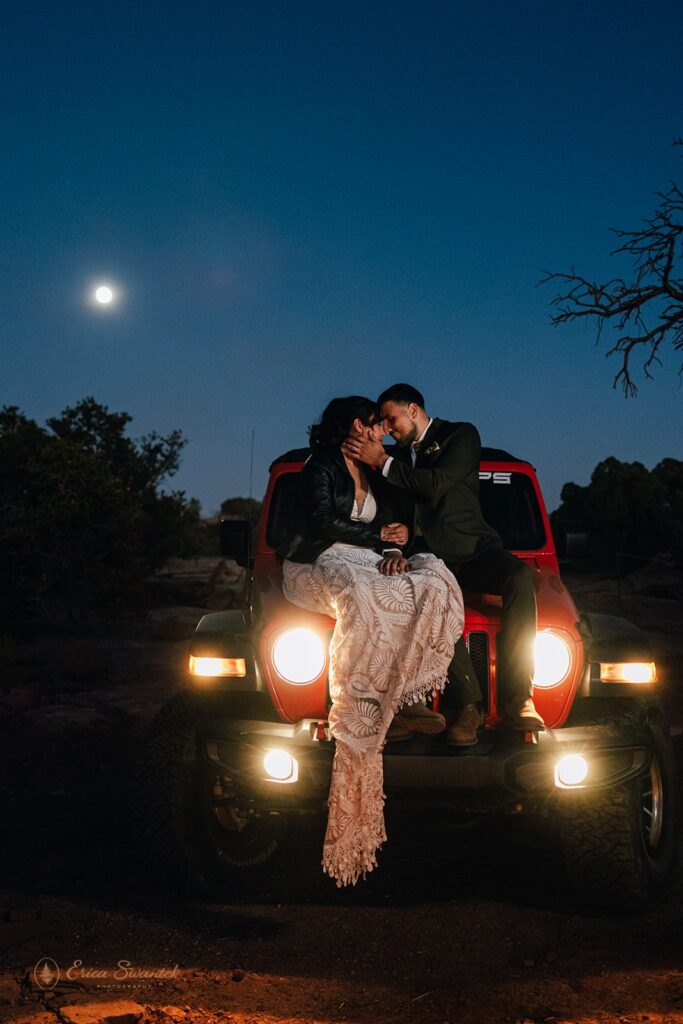 bride and groom sitting on the hood of the jeep with full moon in the background