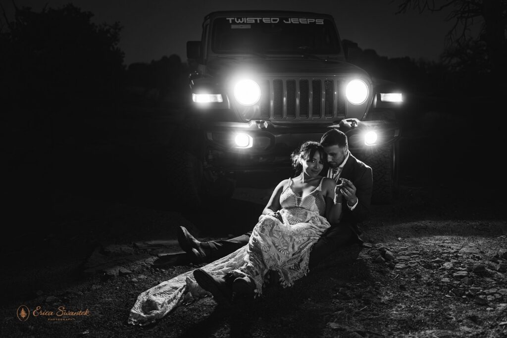 bride and groom sitting in front of the jeep with headlights on