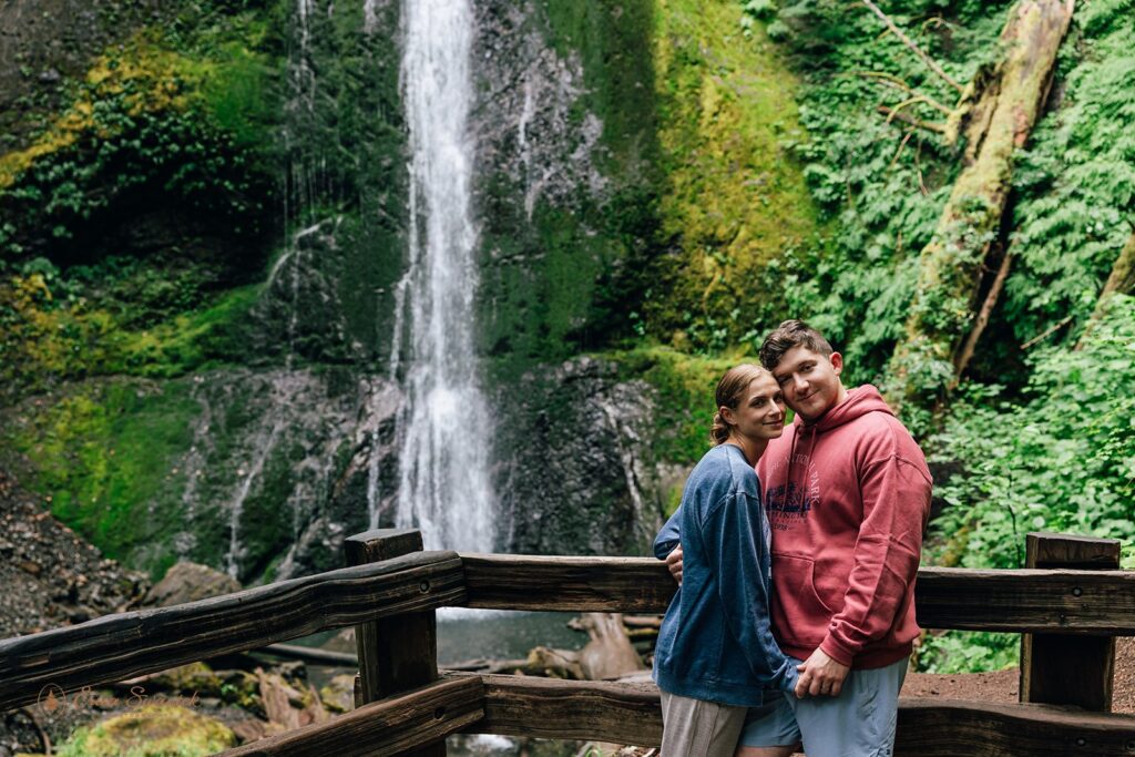 playful couple surrounded by lush forest in front of a waterfall