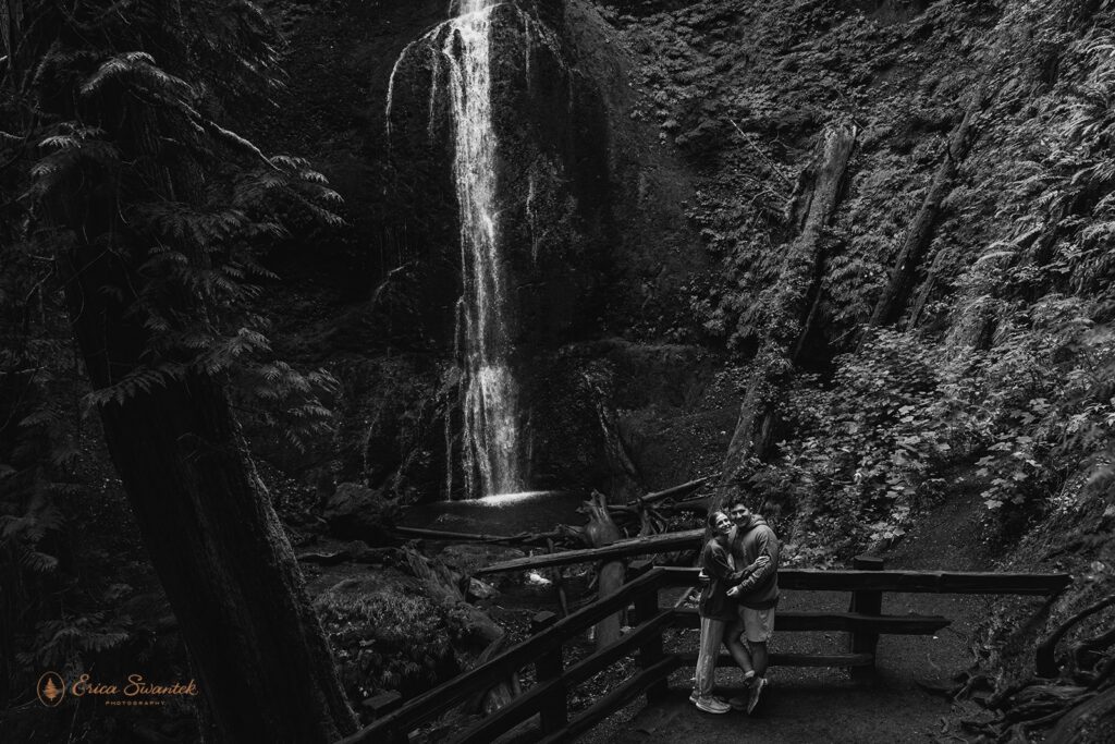 playful couple surrounded by lush forest in front of a waterfall