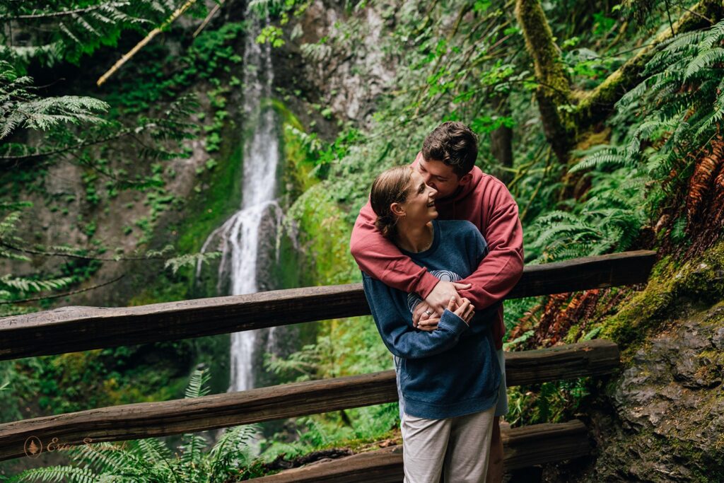 playful couple surrounded by lush forest in front of a waterfall