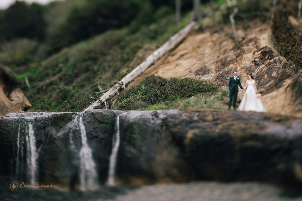 bride and groom walking on top of a small waterfall in pnw
