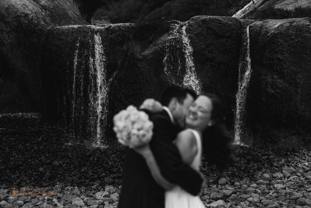 bride and groom hugging in front of a waterfall during their pnw waterfall elopement