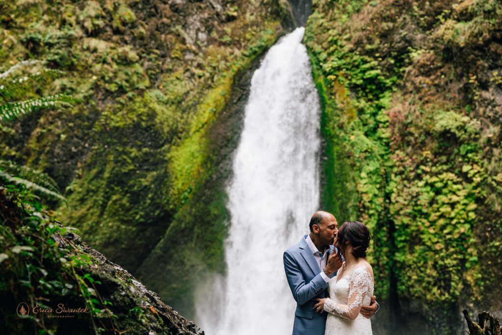bride and groom kissing in front of a waterfall 