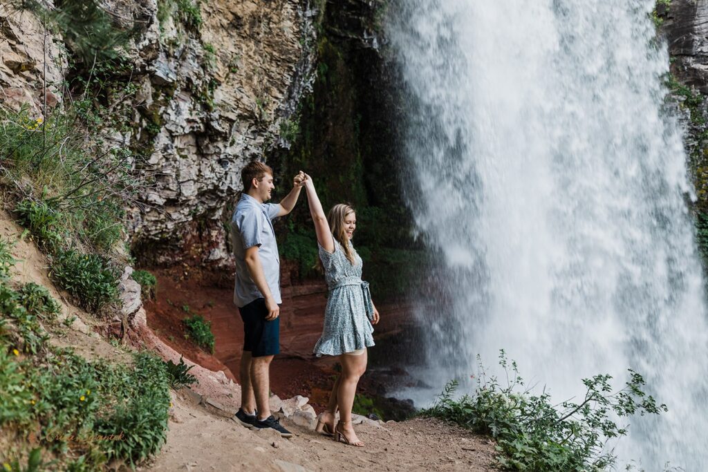 sweet, playful couple getting soaked in front of a waterfall during their session in pnw