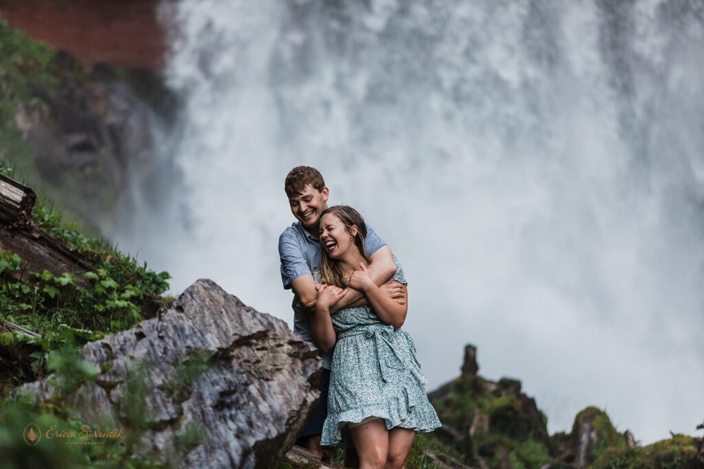 sweet, playful couple getting soaked in front of a waterfall during their session in pnw
