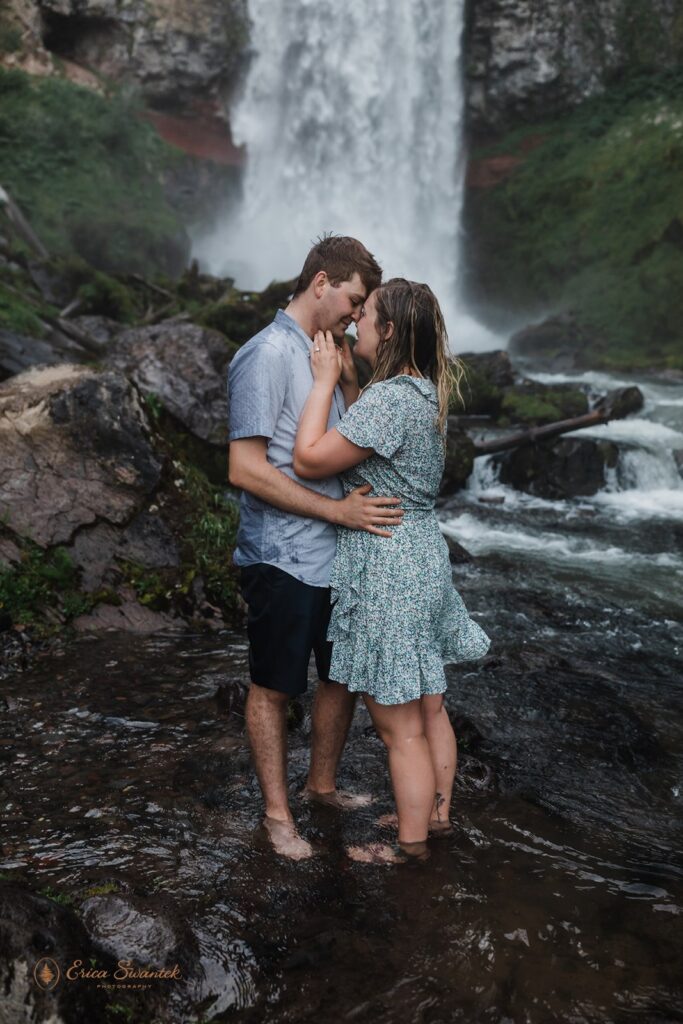 sweet couple getting soaked in front of a waterfall during their session in pnw