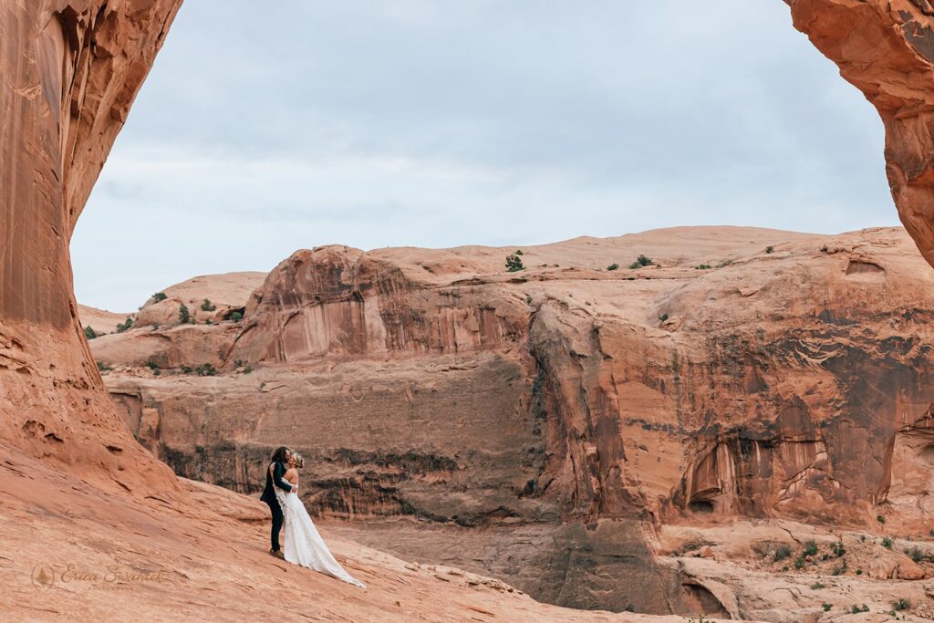 bride and groom kissing at corona arch in moab