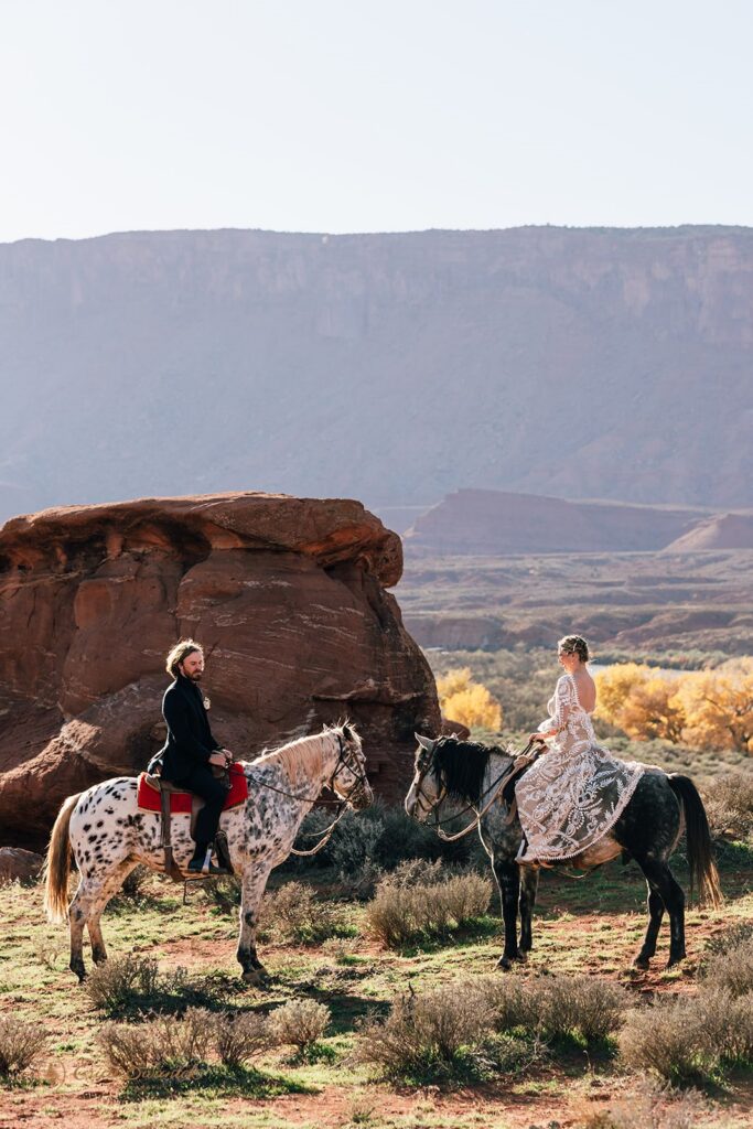 bride and groom horseback riding during their western elopement in moab