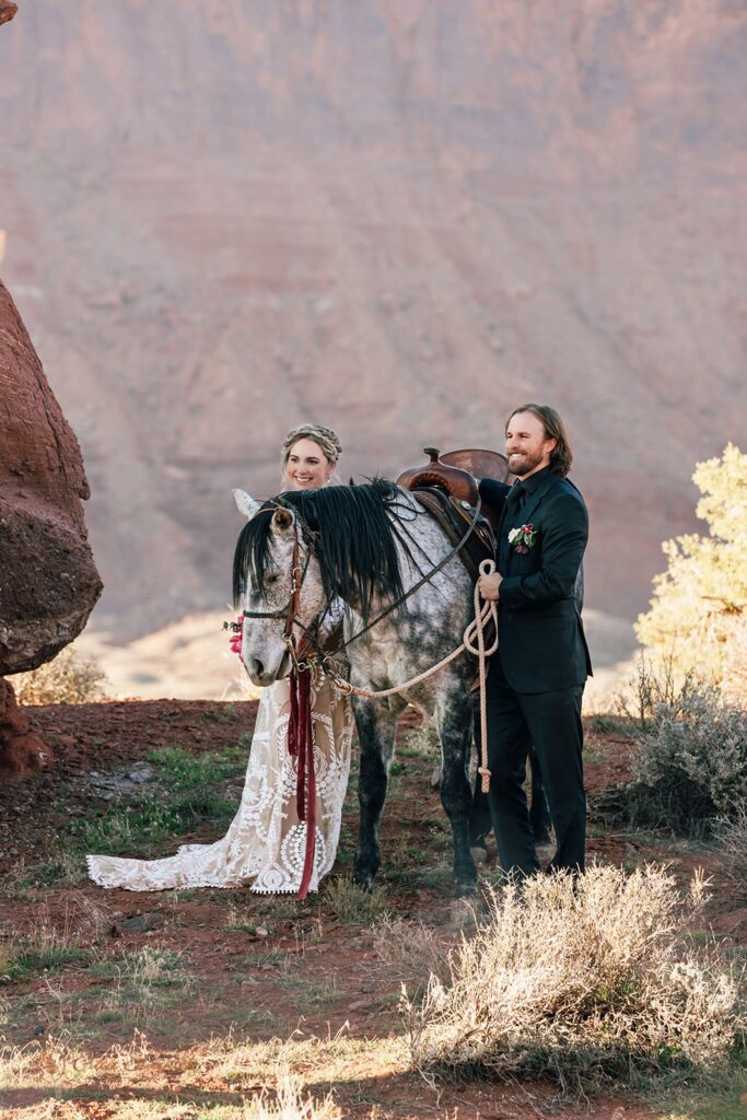 elopement couple posing with a horse during their western horseback riding elopement in moab