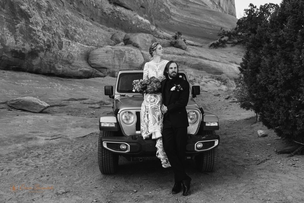 bride and groom sitting on the hood of their jeep