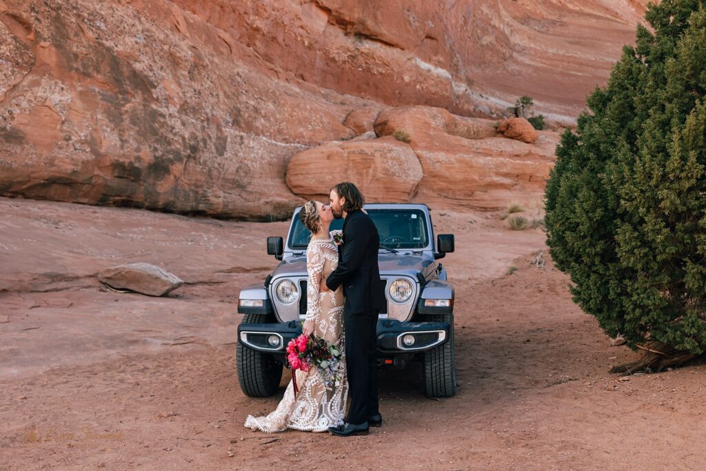 bride and groom kissing in front of their jeep