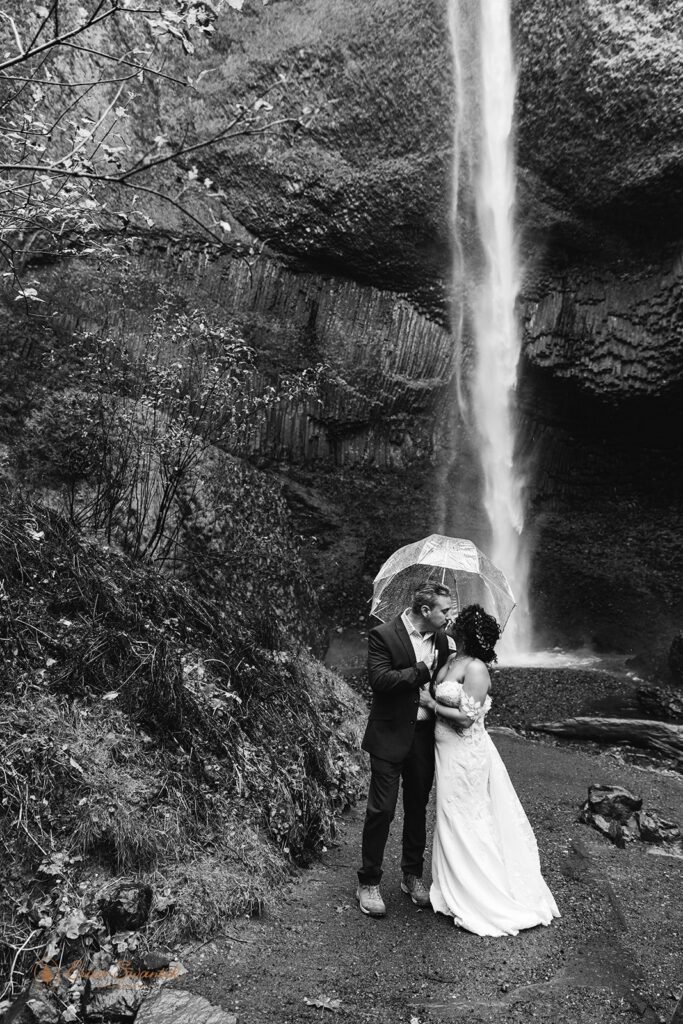 bride and groom holding umbrellas in front of a waterfall
