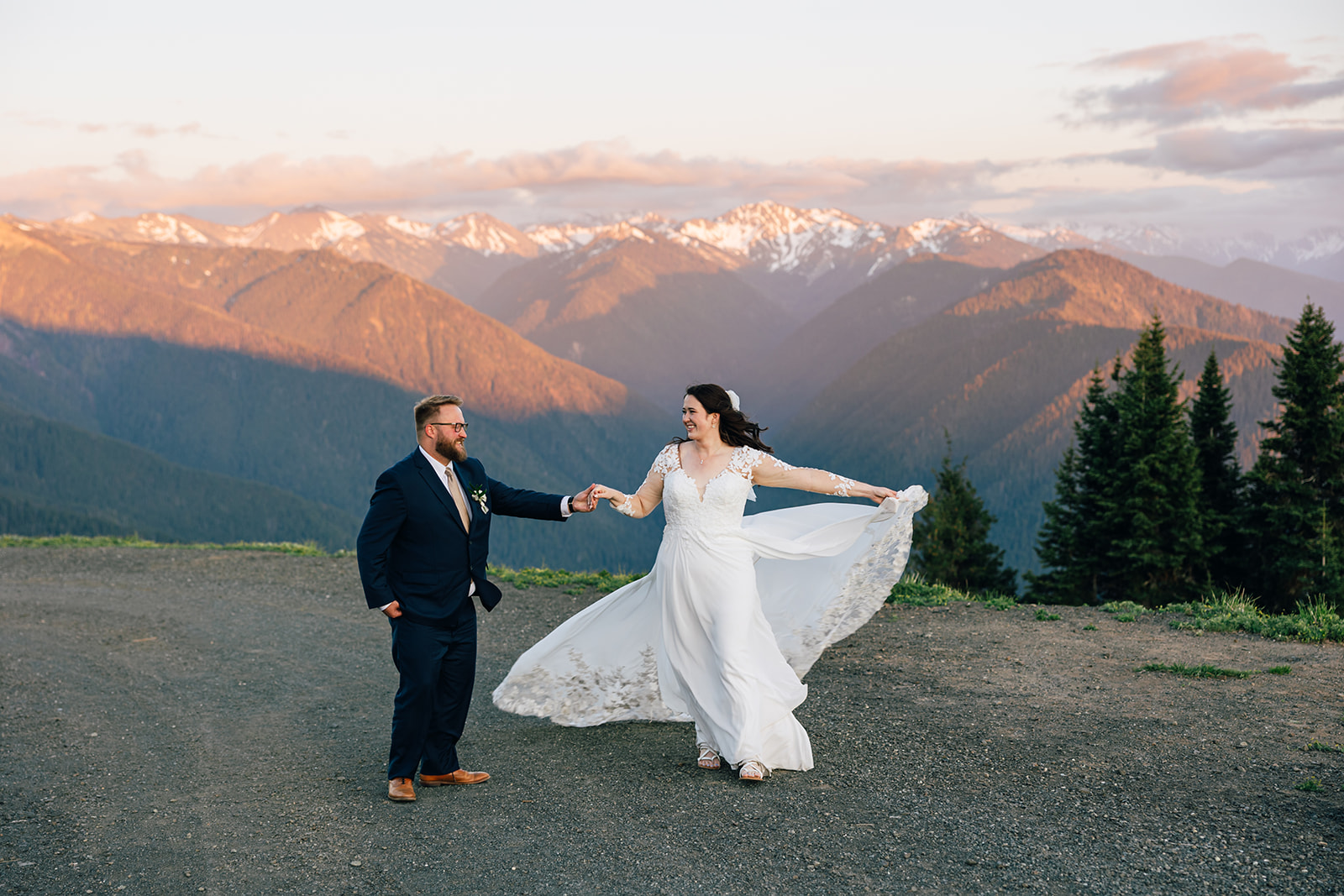 A bride in a white gown is twirled by her husband as the alpenglow hits the mountains on Hurricane Ridge at their Two Day Intimate Wedding in Olympic National Park.