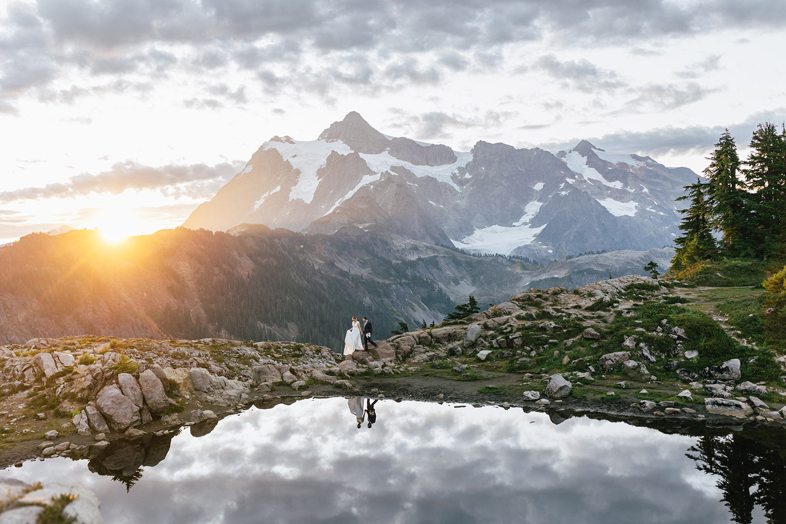 A couple walks along a trail with a mountain behind them at their North Cascades National Park elopement.