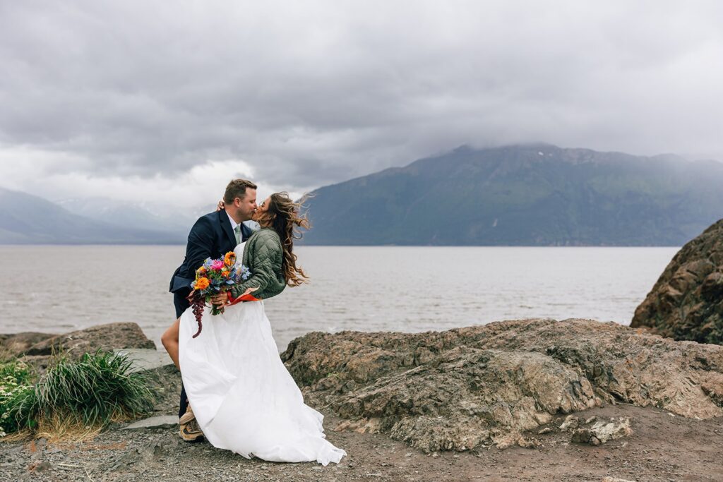 elopement couple kissing in front of a lake with mountain views in alaska 