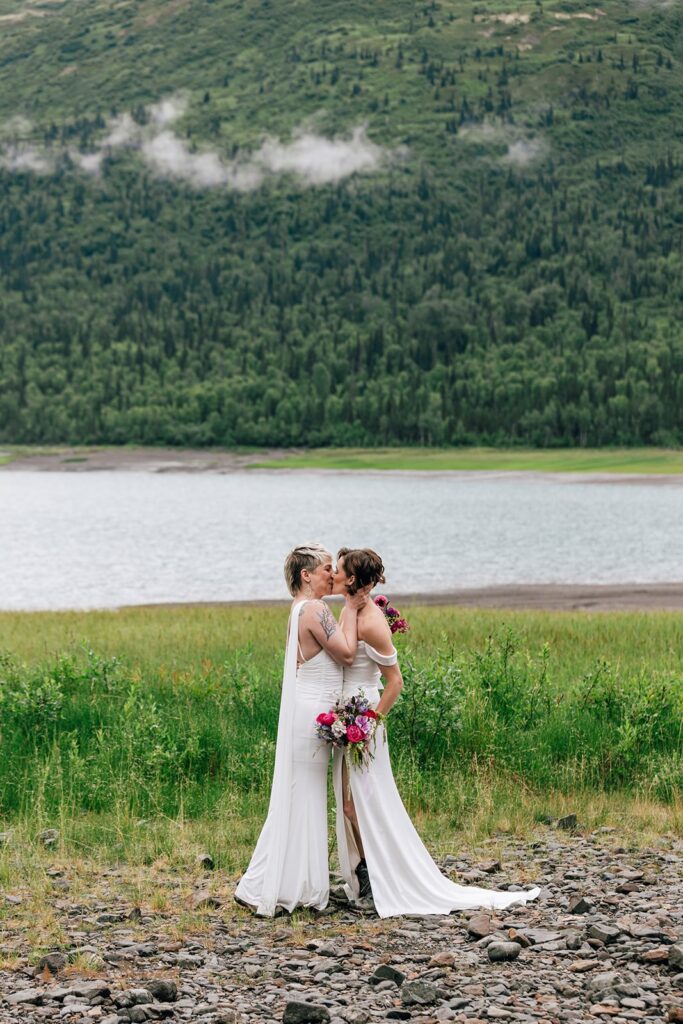 two brides kissing next to a lake in alaska