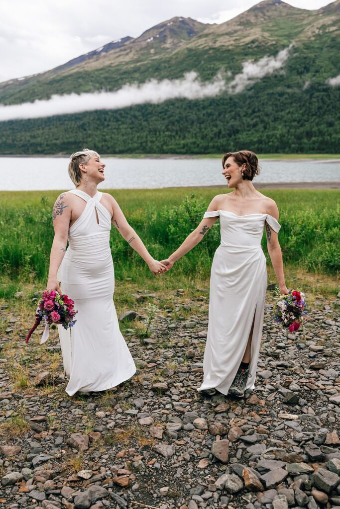 two brides holding hands next to a lake in alaska